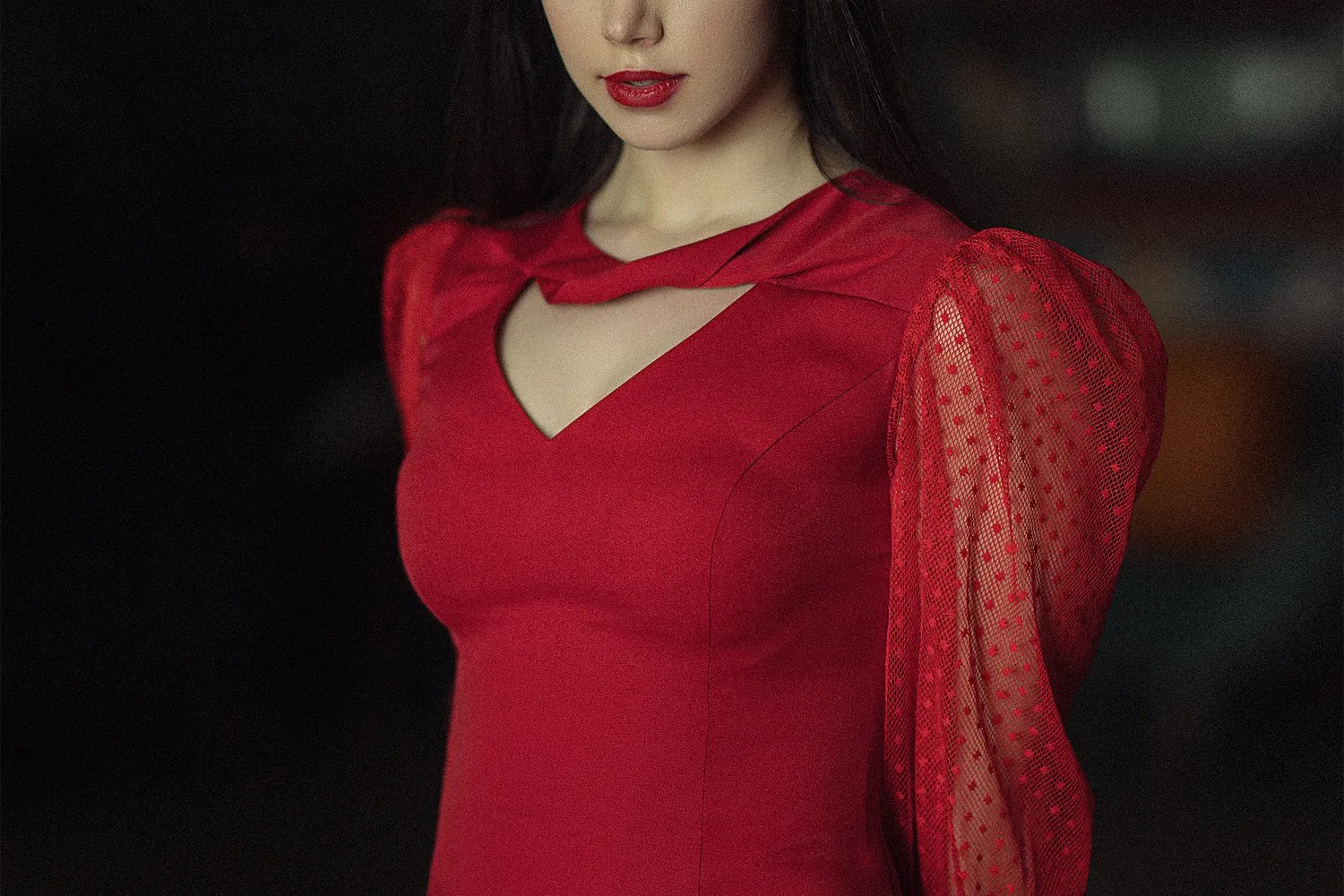 Woman wearing a scarlet evening dress with sheer dotted sleeves and a keyhole neckline