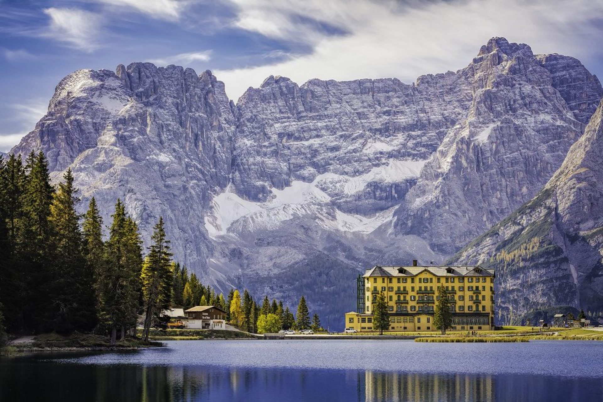 Aurelia Peak Lodge on the shore of a still alpine lake, beneath towering snow-dusted peaks