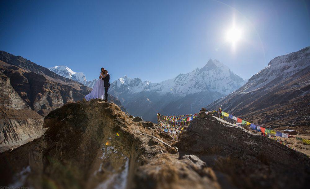 A couple in wedding dress embracing on a ridge in the Annapurna mountains above Pokhara, prayer flags nearby