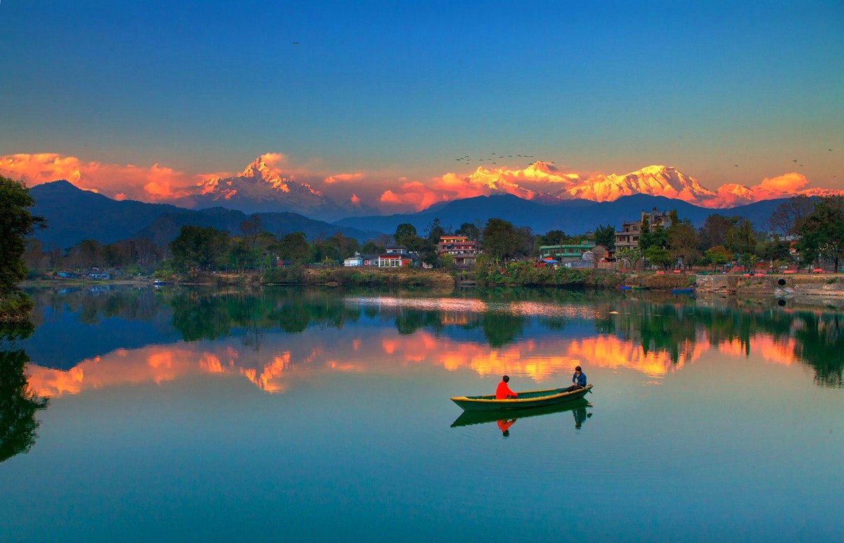 A couple in a wooden boat on Phewa Lake at sunset during their pre-wedding shoot, with the Annapurna range reflected in the water