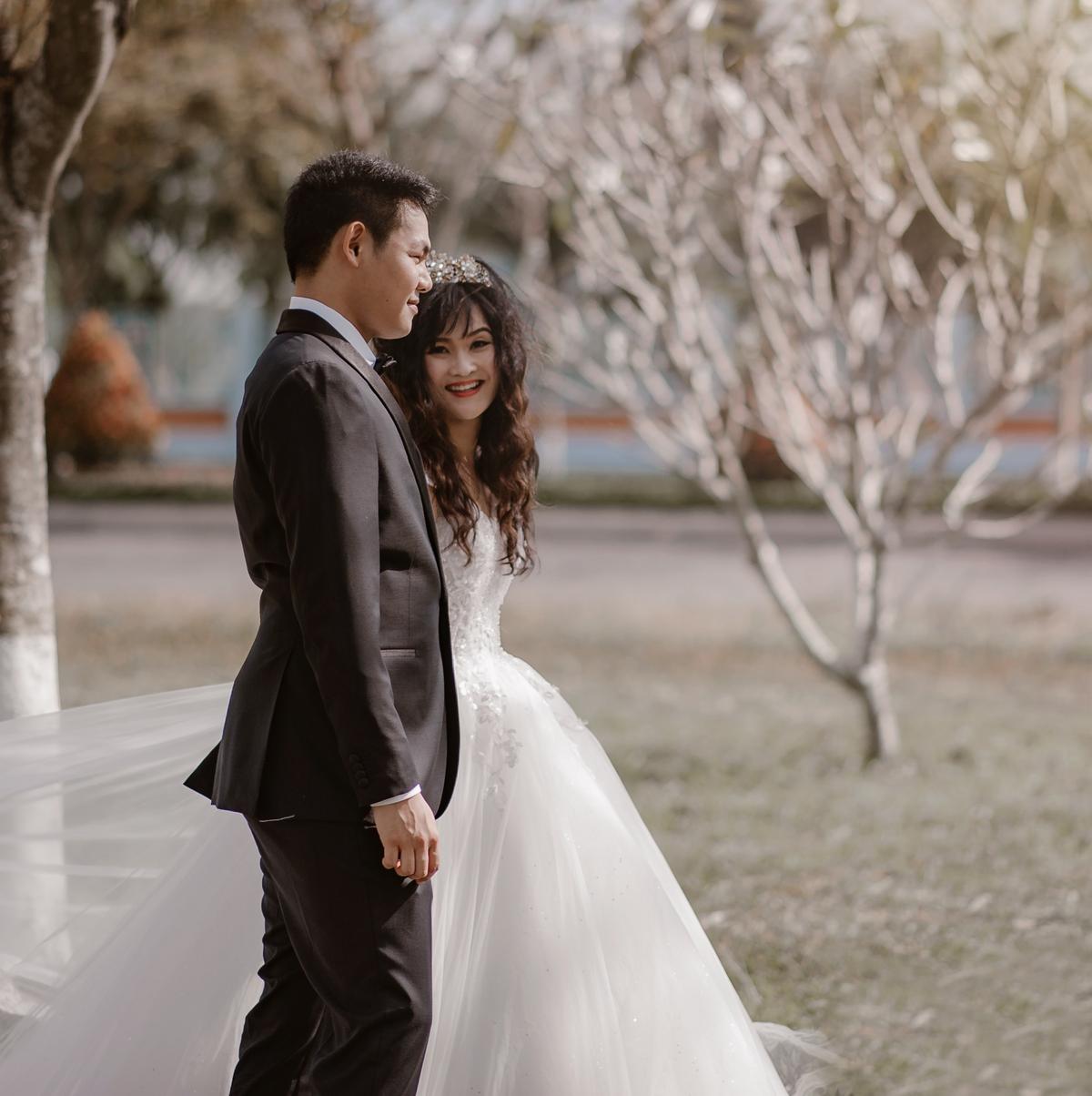 Close portrait of a smiling bride peeking from behind the groom outdoors