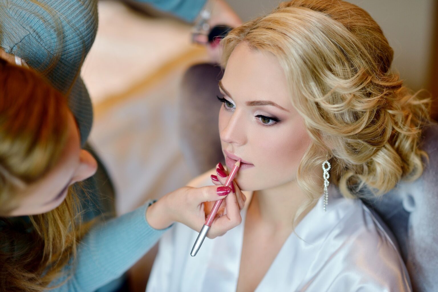 Makeup artist finishing a bride's lip colour, her hair in soft curls