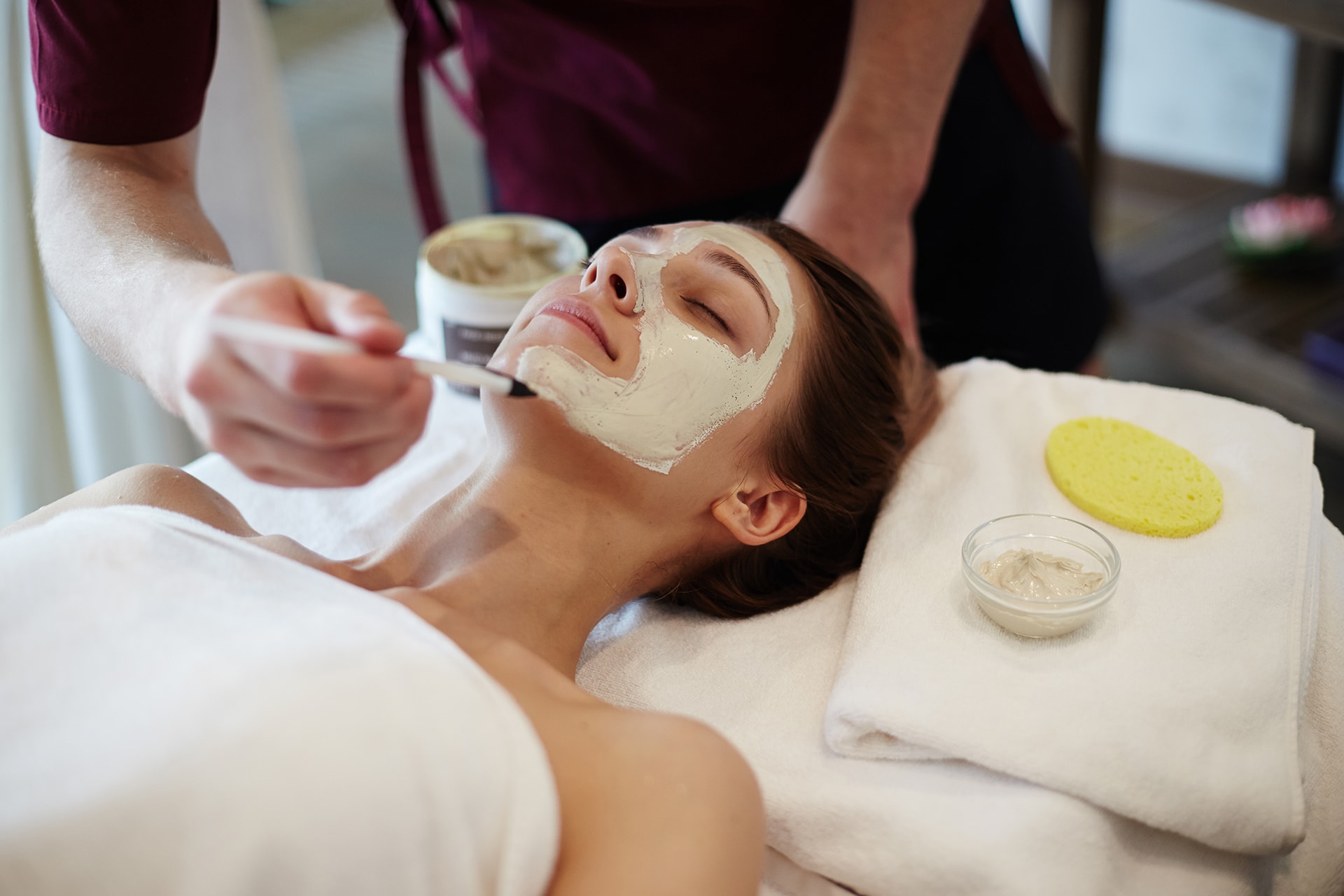 Esthetician applying a clay facial mask to a relaxed client